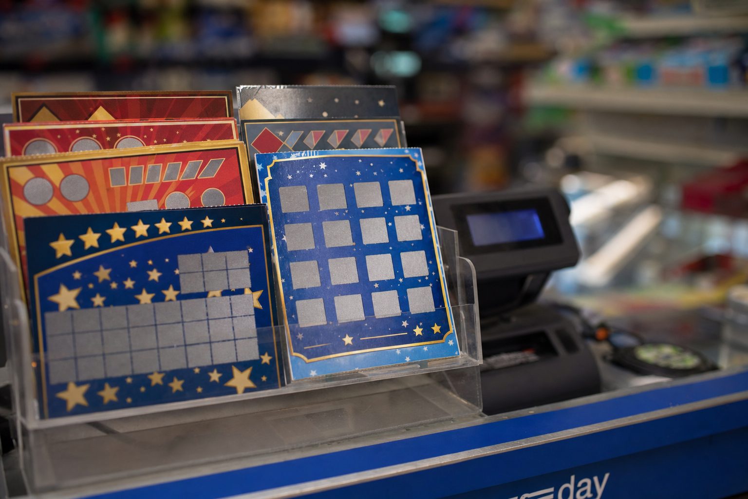 Illustrative newsagent counter display of instant-win scratch cards in a perspex holder